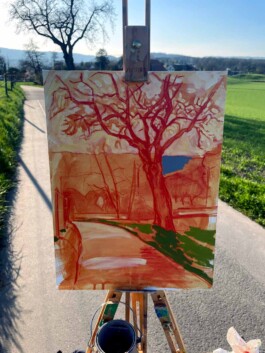 Auf einer Feldstaffelei ist eine kleine Leinwand eingespannt. Darauf sieht man einen Baum in rot skizziert. Im Hintergrund steht die Vorlage – der echte Baum. 